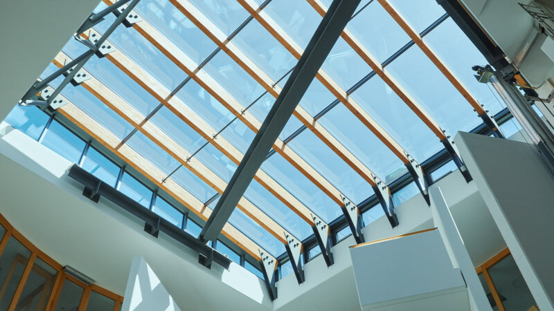 Fachoberschule | Kempten • Aufwendige Sanierung eines 80 m² großen Atriums mit dem System Glasline. Die primäre Holzkonstruktion wurde passgenau mit einer sekundären Aluminiumkonstruktion ergänzt. Die Rauchabzüge sind unauffällig in die Kopfseiten integriert.